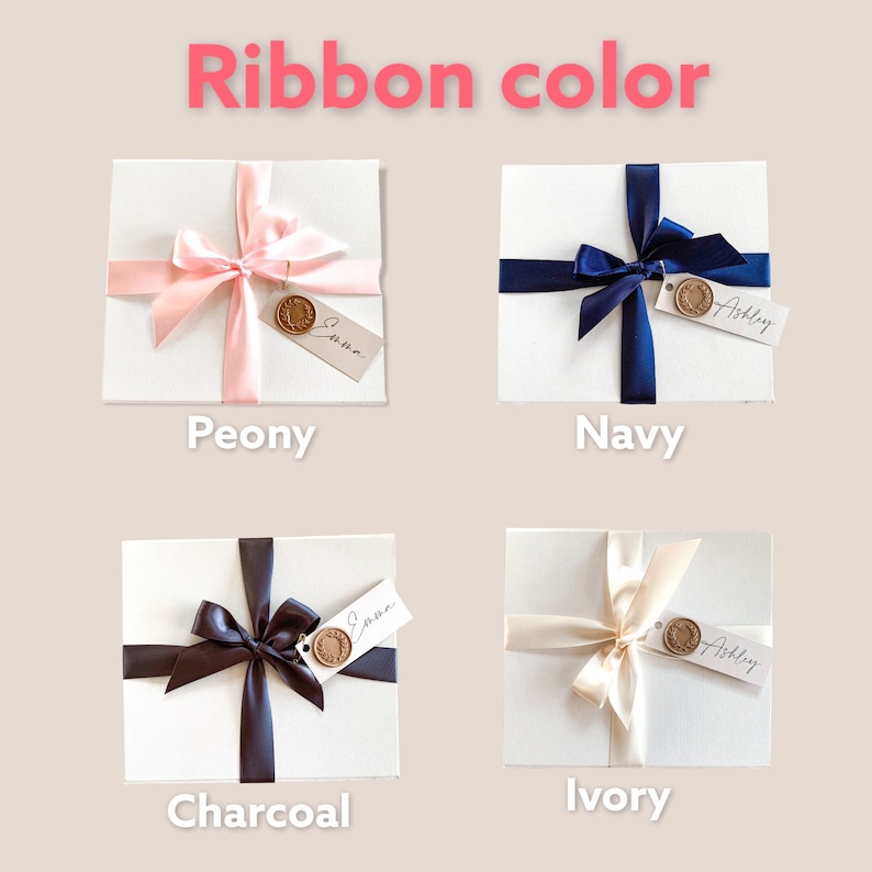 May include: Four white gift boxes with different colored ribbons. The ribbons are peony, navy, charcoal, and ivory. Each box has a tag with the name "Emma" and "Ashley" written on them.
