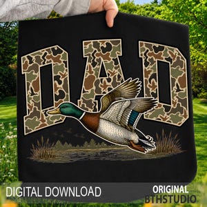 May include: Black tote bag with the word "DAD" in camouflage lettering. A detailed illustration of a flying mallard duck is featured below the text. The words "DIGITAL DOWNLOAD" and "ORIGINAL BTHSTUDIO" are at the bottom.