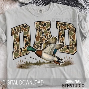 May include: A light grey t-shirt with the word "DAD" in a camouflage design and a black border. Below is a detailed illustration of a flying duck over a lake. The text "DIGITAL DOWNLOAD" and "ORIGINAL BTHSTUDIO" are at the bottom of the shirt.