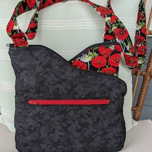 May include: A black crossbody bag with a red zip and a floral print. The strap is made of black fabric with red poppy flowers.
