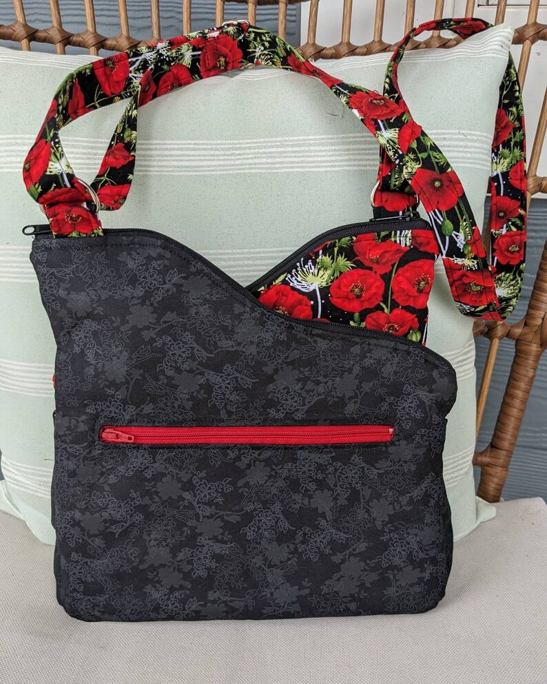 May include: A black crossbody bag with a red zip and a floral print. The strap is made of black fabric with red poppy flowers.