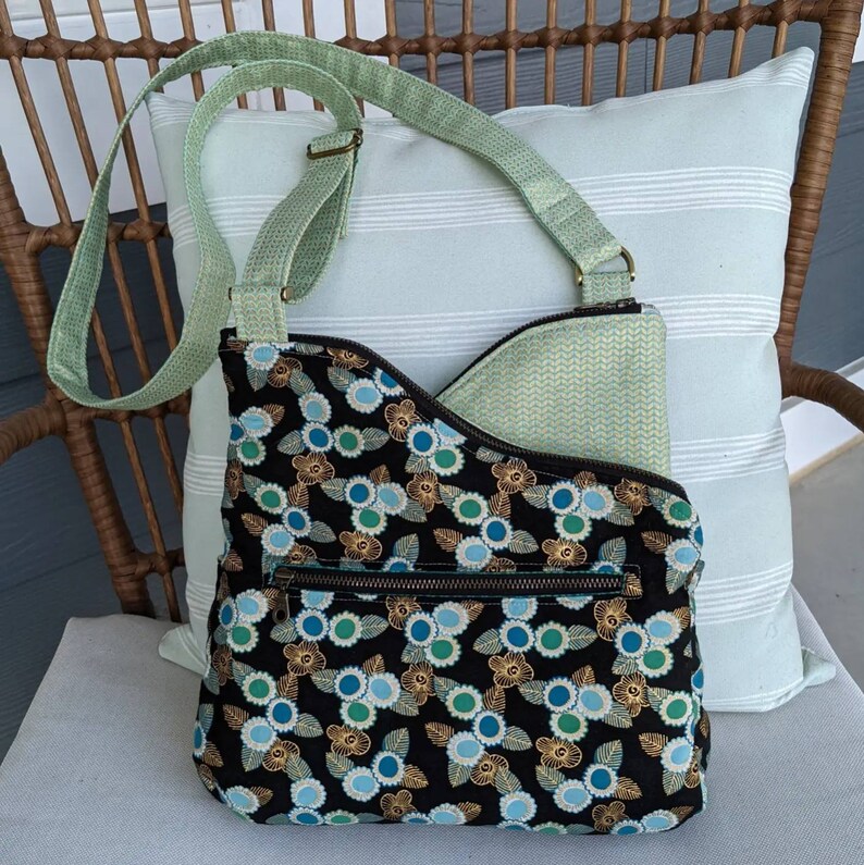 May include: A black and green crossbody bag with a floral pattern and a green strap. The bag has a zipped pocket on the front.