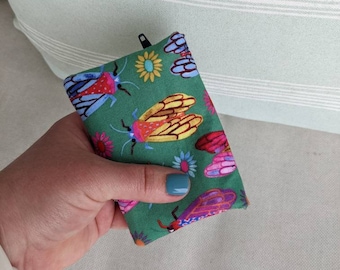 May include: A small green zippered pouch with a colourful print of butterflies and flowers. The pouch is made of fabric and has a zipper closure.