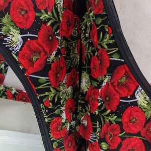 May include: A black fabric bag with a zipper closure and a poppy floral print. The bag has a black zipper and two silver poppers.