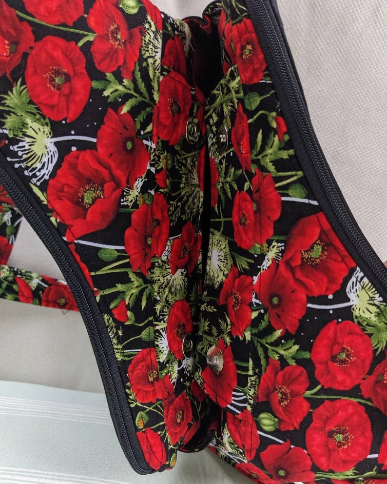 May include: A black fabric bag with a zipper closure and a poppy floral print. The bag has a black zipper and two silver poppers.