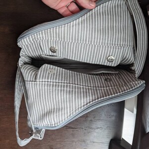 May include: A grey and white striped fabric tote bag with a zipper closure and a long strap. The bag has two pockets on the inside and a snap closure.