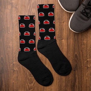 May include: A pair of black socks with a red car pattern. The socks are on a wooden surface.