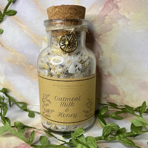 May include: A glass jar with a cork lid filled with a white bath soak. The jar has a brown label that reads "Oatmeal Milk & Honey".