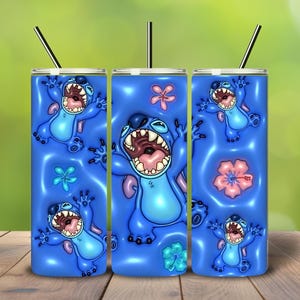May include: Three blue insulated tumblers with a cartoon character design. The design features a blue alien with an open mouth, surrounded by flowers. Each tumbler has a black straw.