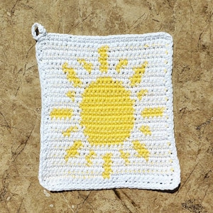 Puede incluir: Paño de cocina de crochet blanco con un diseño de sol amarillo.