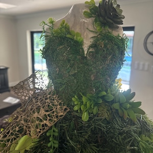 May include: An artificial Christmas tree decorated with moss, greenery, and a small succulent.