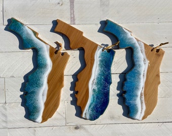 May include: Three wooden chopping boards shaped like the state of Florida with a blue and white ocean wave design.