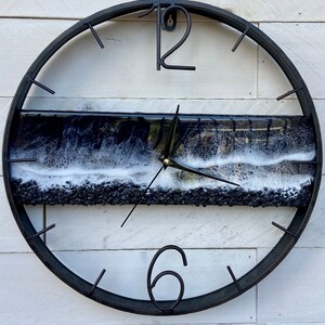 May include: A black metal clock with a white and black resin wave design. The clock face has black Roman numeral markings and black hands.