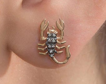 May include: Gold scorpion earring with black diamond accents. The scorpion is detailed with a curled tail and claws.