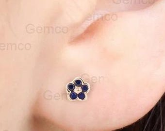 Puede incluir: Un par de pequeños pendientes de botón de flor de oro con esmalte azul. La flor tiene una pequeña piedra transparente en el centro.