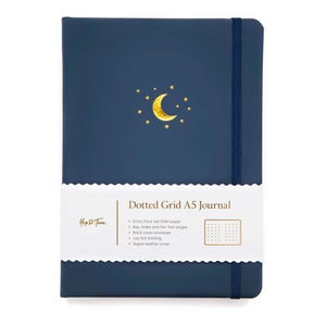 May include: A navy blue A5 dotted grid journal with a gold crescent moon and star design. The journal has a matching elastic band closure and a white paper band with the text "Dotted Grid A5 Journal". The journal features 160 GSM paper and a vegan leather cover.
