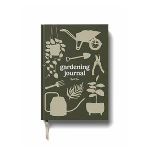Op de afbeelding: Een hardcover tuinjournaal met een donkergroene kaft met witte illustraties van tuingereedschap en planten. De woorden "gardening journal" zijn in het wit gedrukt. Een cr&egrave;mekleurig lint-bladwijzer is bevestigd.