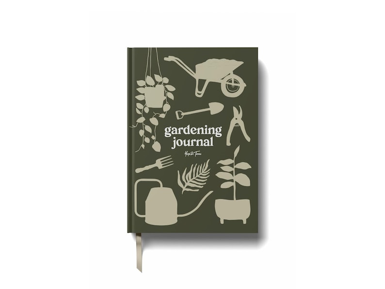 Op de afbeelding: Een hardcover tuinjournaal met een donkergroene kaft met witte illustraties van tuingereedschap en planten. De woorden "gardening journal" zijn in het wit gedrukt. Een cr&egrave;mekleurig lint-bladwijzer is bevestigd.