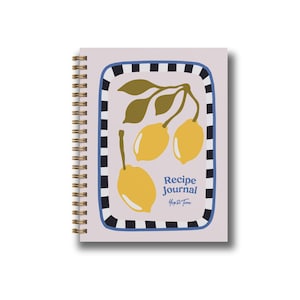 May include: A spiral-bound recipe journal with a light purple cover. The cover features a rectangular design with a black and white border, enclosing a lemon illustration and the words "Recipe Journal".