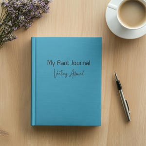 Puede incluir: Un diario azul con el texto "My Rant Journal Venting Allowed" en la portada. El diario está sobre una mesa de madera con un bolígrafo y una taza de café.