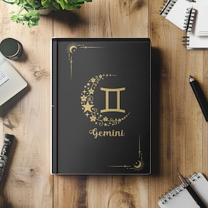 May include: Black journal with a gold crescent moon and stars design. The journal features the Gemini zodiac symbol and the word "Gemini" in gold lettering.