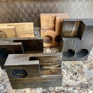 May include: Four wooden cup holders in various sizes and finishes. Two are dark brown with two cup holders each, one is light brown with two cup holders, and one is dark brown with one cup holder.