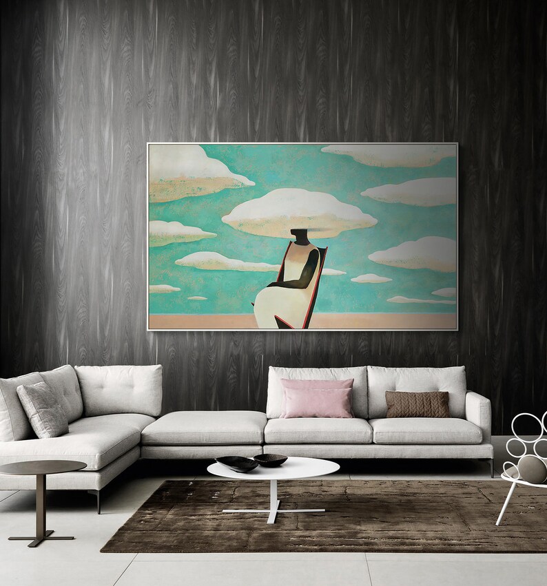 May include: A white sofa with a pink throw pillow and a brown throw pillow. A white coffee table sits in front of the sofa. A framed painting of a person sitting on a chair with clouds above their head hangs on the wall behind the sofa.