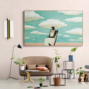 May include: A brown couch with two pillows sits in a living room with a large painting of a person sitting on a chair with clouds above their head. The painting is framed in gold and has a light blue background. There are plants and a small table in the room.