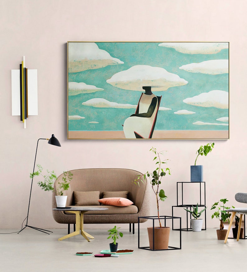 May include: A brown couch with two pillows sits in a living room with a large painting of a person sitting on a chair with clouds above their head. The painting is framed in gold and has a light blue background. There are plants and a small table in the room.