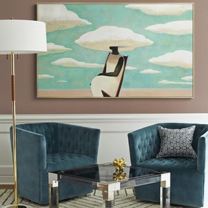 May include: A teal blue velvet armchair with a tufted back and a black and white geometric patterned pillow sits next to a similar armchair. A glass coffee table with a black top and silver legs sits between the two chairs. A gold metal sculpture sits on the table. A gold floor lamp with a white shade stands in the corner of the room. A painting of a person sitting in a chair with clouds above their head hangs on the wall.