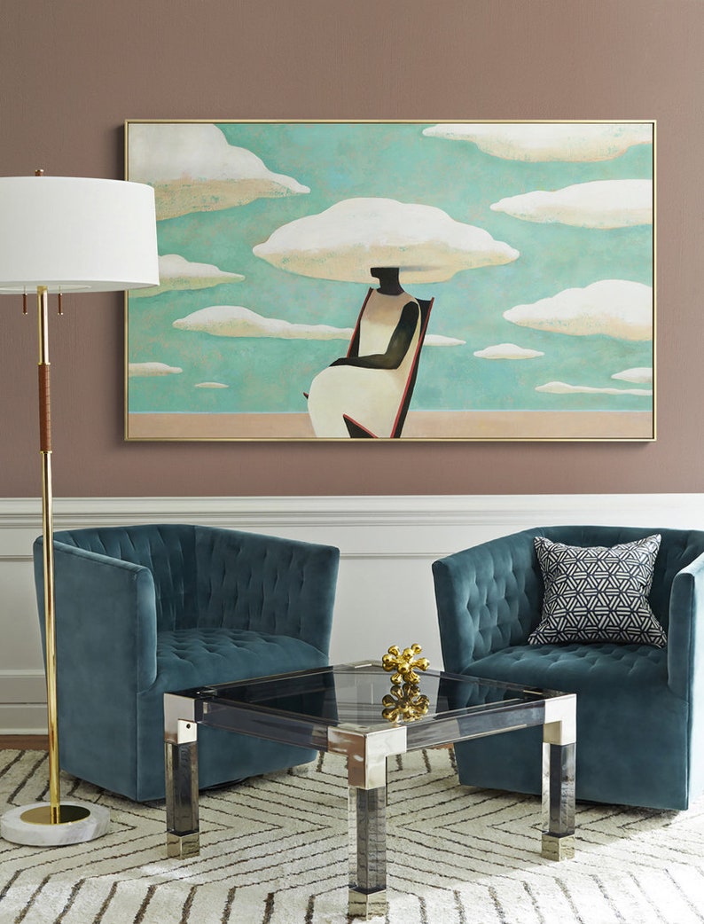 May include: A teal blue velvet armchair with a tufted back and a black and white geometric patterned pillow sits next to a similar armchair. A glass coffee table with a black top and silver legs sits between the two chairs. A gold metal sculpture sits on the table. A gold floor lamp with a white shade stands in the corner of the room. A painting of a person sitting in a chair with clouds above their head hangs on the wall.