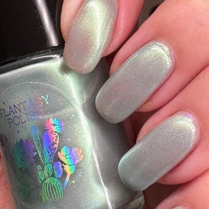 May include: A bottle of light green nail polish with a holographic shimmer. The bottle has a label that says "Plantaby Polish" and features a cactus design.