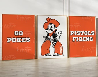 May include: Set of three framed art prints. The left and right prints are orange with white text that reads "GO POKES" and "PISTOLS FIRING". The center print features a cowboy mascot in orange and black on a white background.