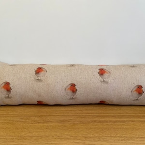 May include: A beige doorstop with a repeating pattern of red robins. The doorstop is made of a soft, textured fabric.