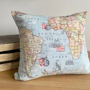 May include: A blue and white cushion featuring a vintage world map design. The map shows continents, oceans, and countries. The cushion is ideal for adding a touch of travel and adventure to any room.