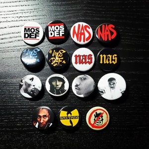 May include: A collection of 12 round button pins featuring various hip hop artists and groups. The pins feature images of Nas, Mos Def, and Wu-Tang Clan. The pins are black, white, red, and yellow.
