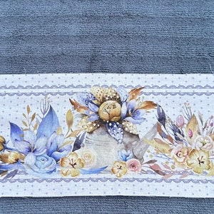 Puede incluir: Una toalla de algod&oacute;n blanca con un dise&ntilde;o floral azul y blanco. El dise&ntilde;o presenta una regadera, flores y hojas. La toalla tiene un fondo blanco con lunares azules y un borde de encaje azul.