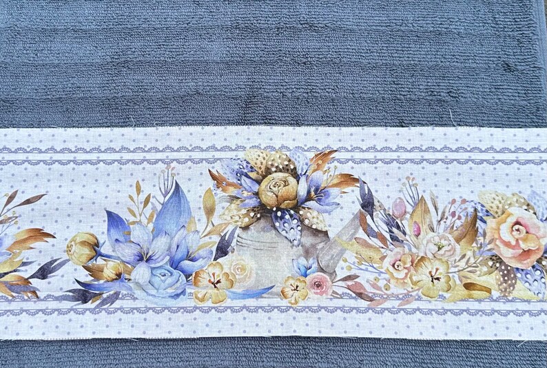 Puede incluir: Una toalla de algod&oacute;n blanca con un dise&ntilde;o floral azul y blanco. El dise&ntilde;o presenta una regadera, flores y hojas. La toalla tiene un fondo blanco con lunares azules y un borde de encaje azul.