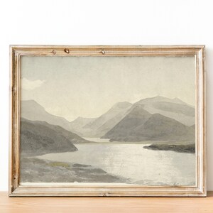 May include: A framed watercolor painting of a mountain lake scene. The painting features a light blue lake surrounded by gray mountains and a light blue sky.