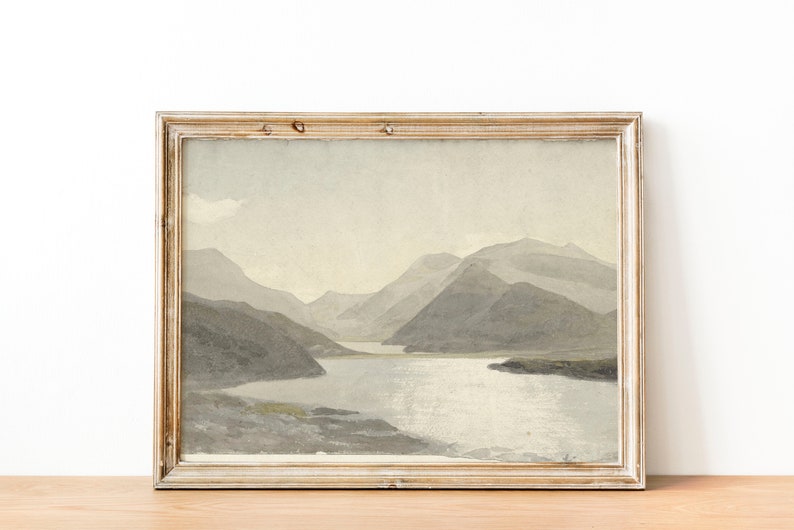 May include: A framed watercolor painting of a mountain lake scene. The painting features a light blue lake surrounded by gray mountains and a light blue sky.