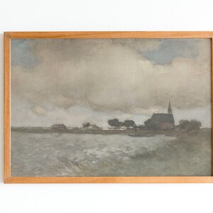 May include: A framed painting depicting a landscape with a church in the distance. The sky is cloudy and gray, and the water in the foreground is choppy. The painting is in a wooden frame.