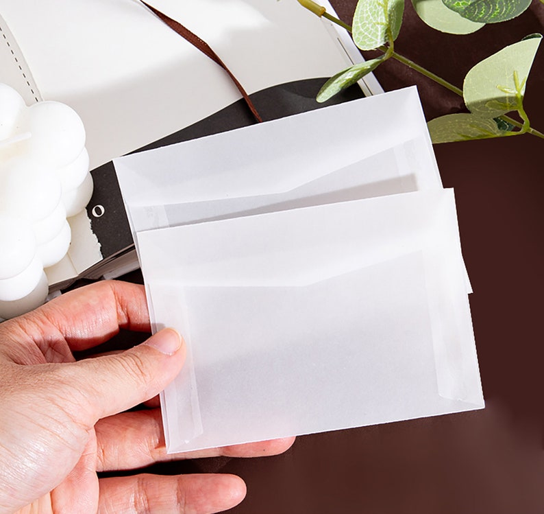 K&ouml;nnte beinhalten: Zwei wei&szlig;e, durchscheinende Umschl&auml;ge, die &uuml;bereinander gestapelt sind. Die Umschl&auml;ge bestehen aus einem d&uuml;nnen, zarten Papier und haben eine leicht strukturierte Oberfl&auml;che.