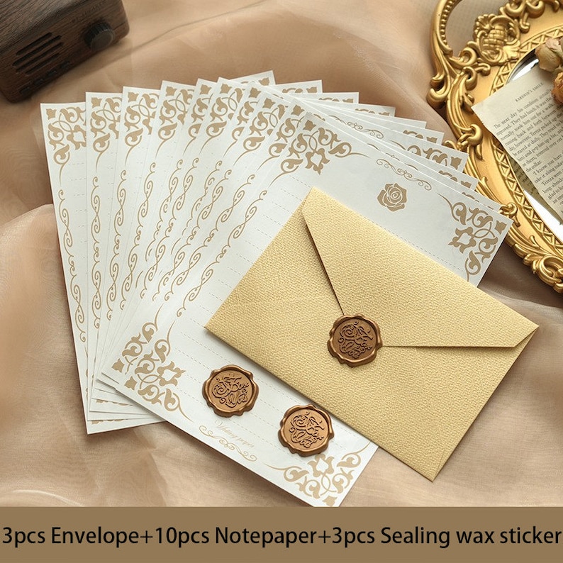 K&ouml;nnte beinhalten: Ein Set aus 10 wei&szlig;en Briefb&ouml;gen mit goldenen, verzierten R&auml;ndern und 3 goldenen Umschl&auml;gen mit einem goldenen Siegelwachsaufkleber. Die Briefb&ouml;gen und Umschl&auml;ge haben ein florales Design. Der Text auf dem Bild lautet "3pcs Envelope+10pcs Notepaper+3pcs Sealing wax sticker".