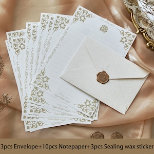 K&ouml;nnte beinhalten: Ein Set aus 10 wei&szlig;en Briefpapierbl&auml;ttern mit goldenen, verzierten R&auml;ndern und 3 wei&szlig;en Umschl&auml;gen mit einem goldenen Wachssiegel. Das Briefpapier hat Linien zum Schreiben und den Text "Writing paper" unten. Die Umschl&auml;ge haben eine strukturierte Oberfl&auml;che.