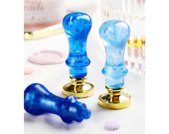May include: Three blue wax seal stamps with gold bases. The stamps have different designs on the top.