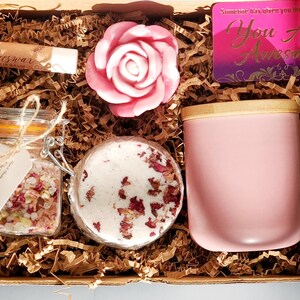 May include: A pink gift box filled with self-care items, including a pink rose soap, a jar of bath salts, a pink candle, and a lip balm. The box also includes a card that says "You Are Awesome!"