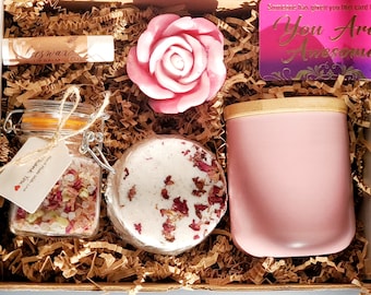 May include: A pink gift box filled with self-care items, including a pink rose soap, a jar of bath salts, a bath bomb, a lip balm, and a pink candle. The box also includes a card that says "You Are Awesome!"