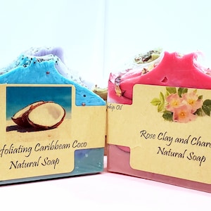 May include: Two bars of natural soap, one blue and purple with a coconut image and the text "Exfoliating Caribbean Coco Natural Soap", and the other pink with a rose image and the text "Rose Clay and Charcoal Natural Soap".