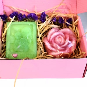 May include: A pink gift box filled with shredded paper, containing a green soap bar with a heart design and a pink rose-shaped soap.