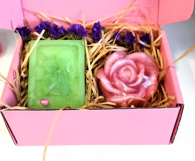 May include: A pink gift box filled with shredded paper, containing a green soap bar with a heart design and a pink rose-shaped soap.